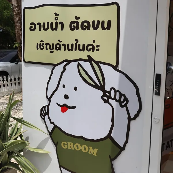 A cartoon dog in a GROOM t-shirt by the front door, under a Thai sign that says bath and haircut, please come in
